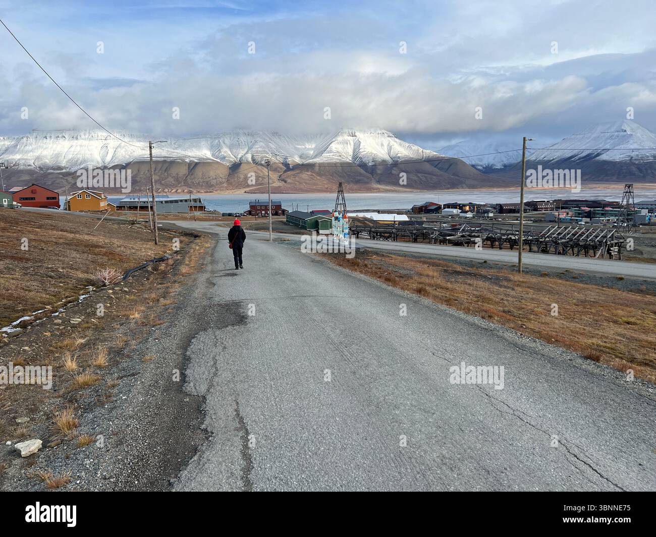 A person walks down a road towards a scenic mountain range on a cloudy day. Longyearbyen Svalbard - Smartphone Captured Stock Image