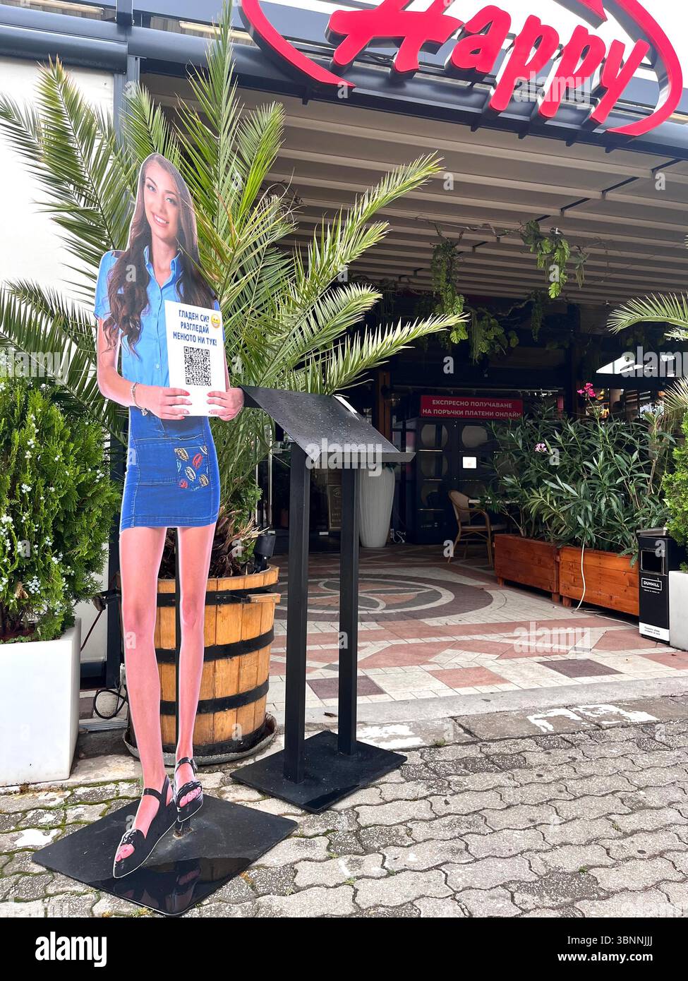 Young woman cardboard cutout employee welcoming customers at the Happy Bar&Grill Restaurant entrance in Sofia Bulgaria, Eastern Europe, Balkans, EU - Smartphone Captured Stock Image