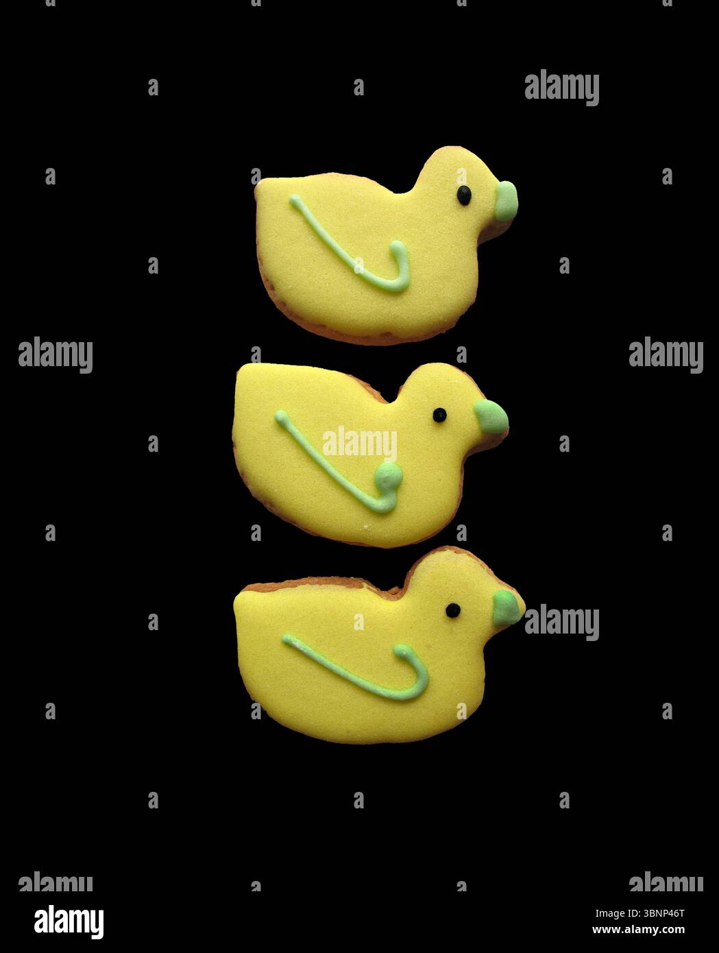 Three yellow duck-shaped biscuits isolated on a black background. Stock Photo
