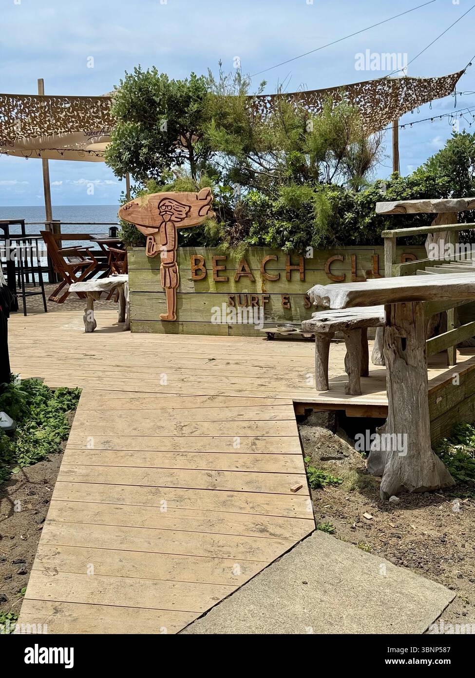 Outdoor seating at a rustic beach club on São Miguel Island, Azores, Portugal. Wooden furniture and natural decor overlook the Atlantic Ocean. - Smartphone Captured Stock Image