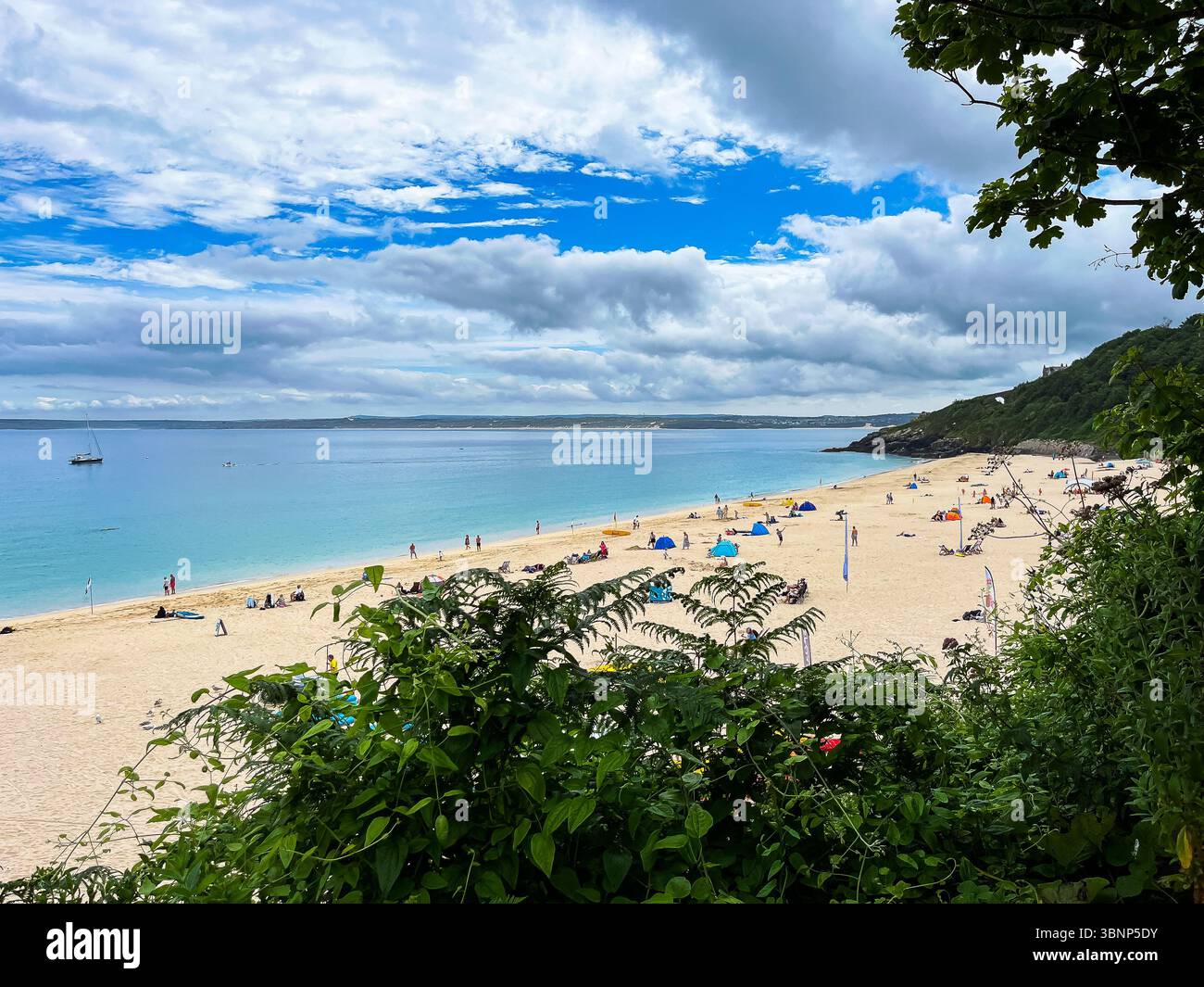 Beachgoers are enjoying a sunny day on the sand and in the water, relaxing under tents, swimming, and taking in the coastal scenery. - Smartphone Captured Stock Image