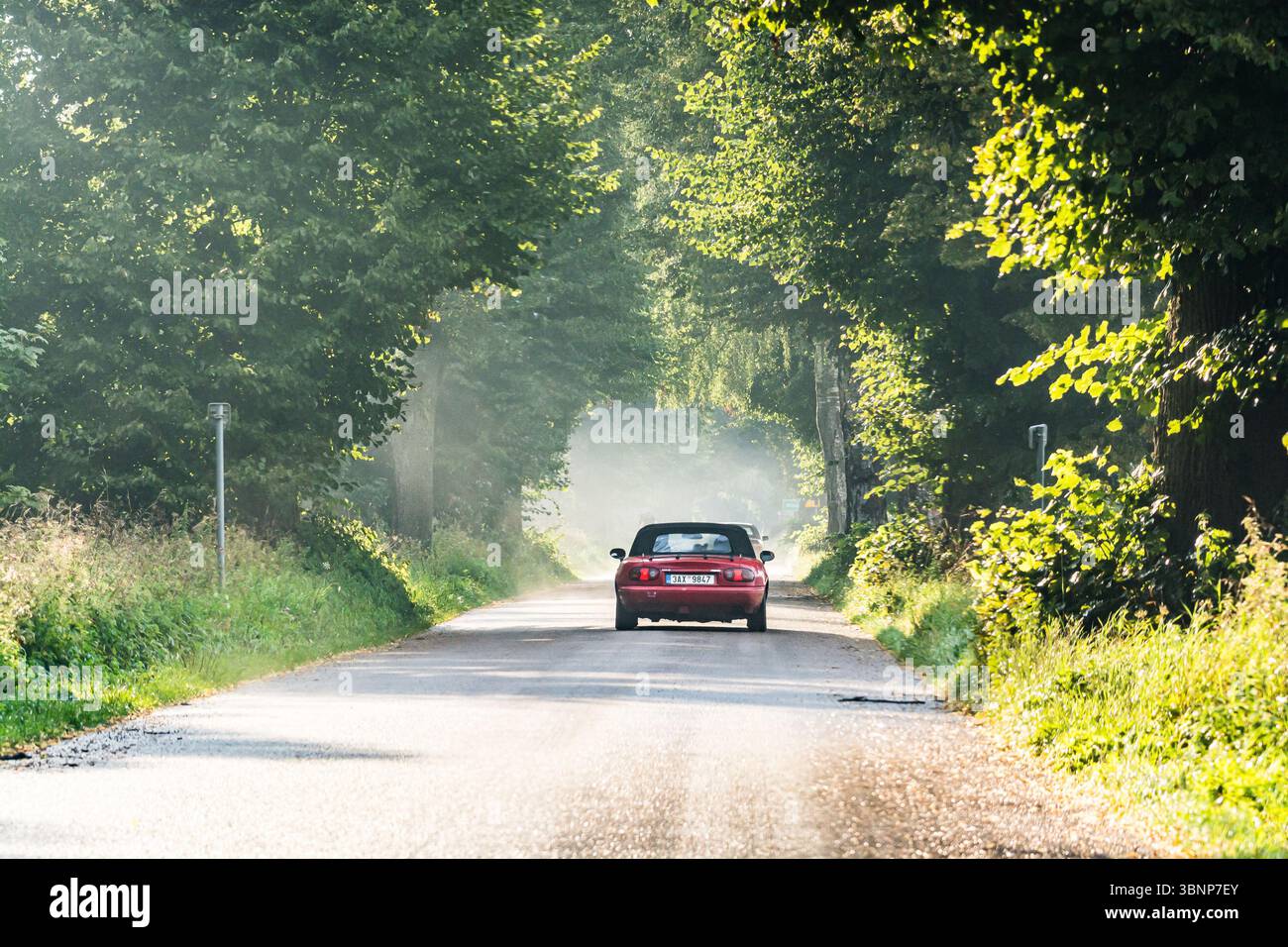 Braniewo, Poland - August 16, 2021. Red convertible Mazda MX5 going on the tar road through parkway in sunset Stock Photo