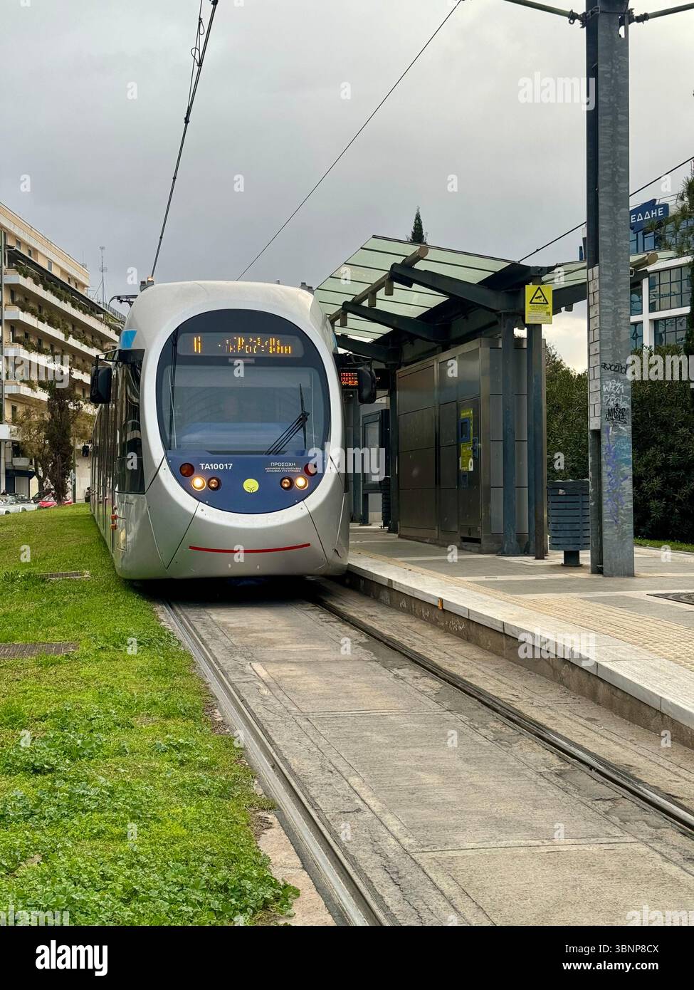 A modern light rail tram at a station in Athens, Greece. The image shows the tram waiting at a platform with overhead electric lines, modern shelter, - Smartphone Captured Stock Image