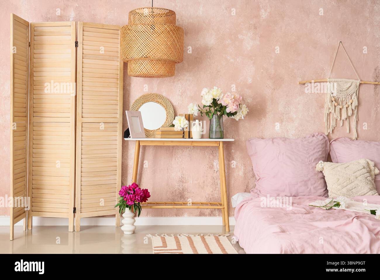 Bedside table with mirror, books and beautiful peonies in bedroom Stock Photo