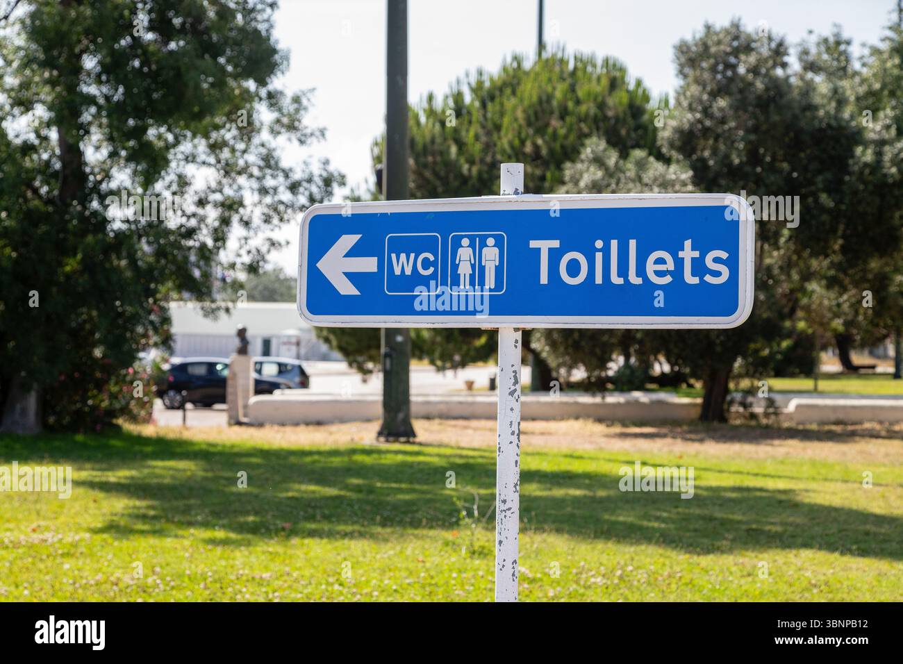 A blue sign with a spelling error for “toilets” points left to public restrooms in a park area in Lisbon, Portugal. Stock Photo