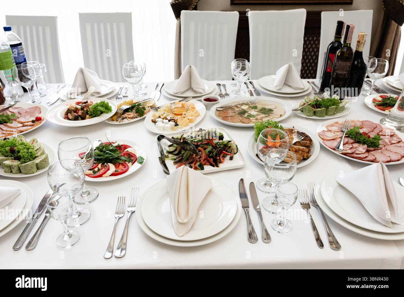 A beautifully arranged banquet table showcases a variety of cold cuts, salads, and appetizers. Elegant place settings and wine bottles complete the sc Stock Photo