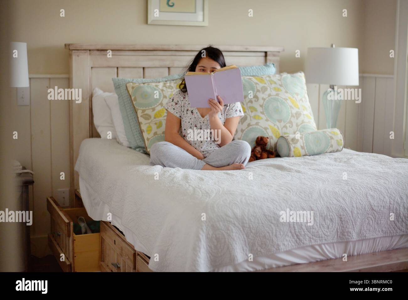 Young woman with down syndrome reading a book in bed Stock Photo