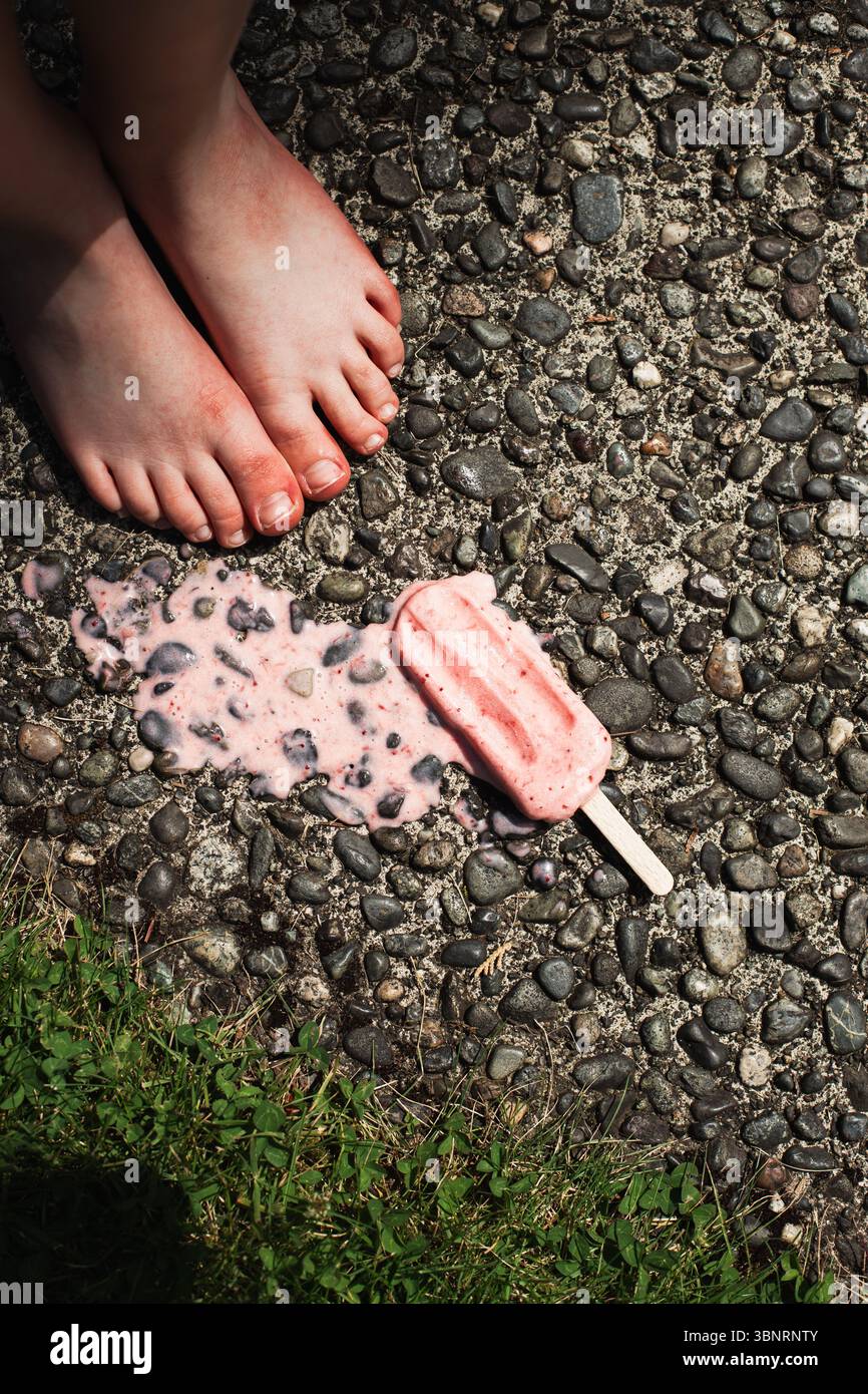 Child's feet standing by melted popsicle Stock Photo