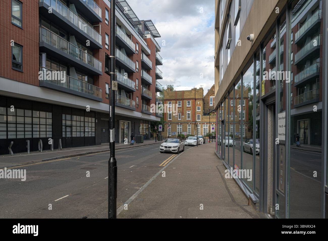 United Kingdom, London, 13 Jul 2025. Quiet residential and office street in Shoreditch with parked cars, modern apartment buildings, and reflected fac Stock Photo