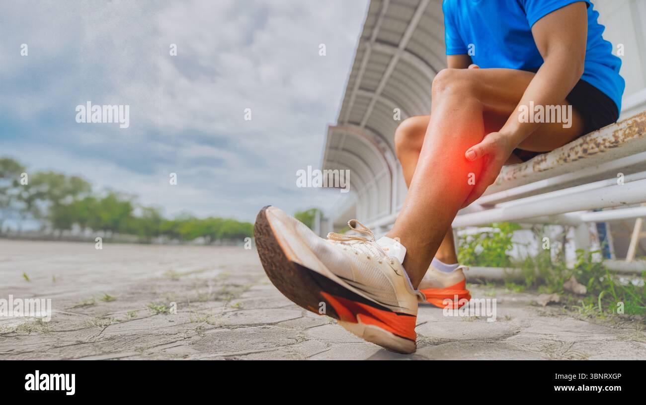 Athlete sitting holding calf muscle with pain after running injury outdoor sports medicine concept Stock Photo