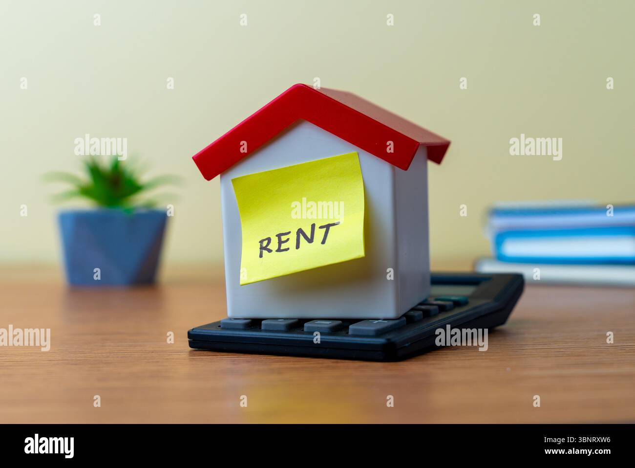 A miniature house on top of a calculator and a yellow sticky note with ...