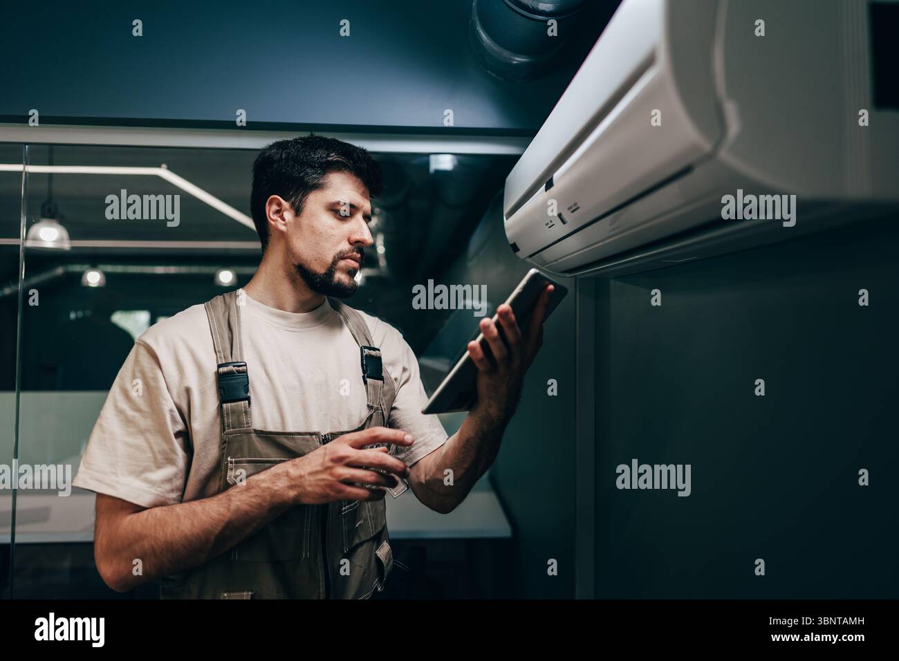 Technician performs maintenance on air conditioning unit while checking data on tablet Stock Photo