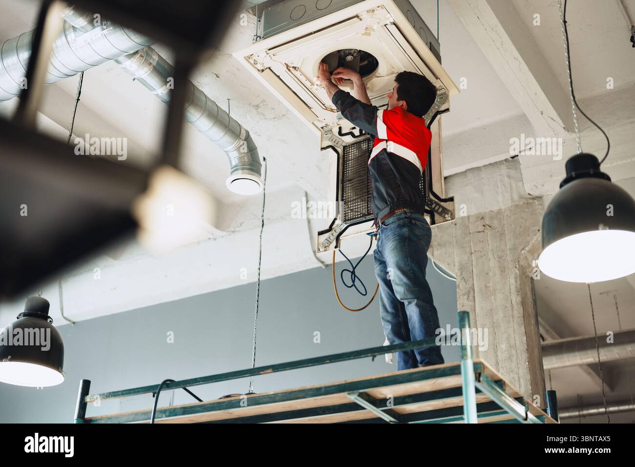 Technician performs installation work on ceiling-mounted air conditioning unit in modern office Stock Photo