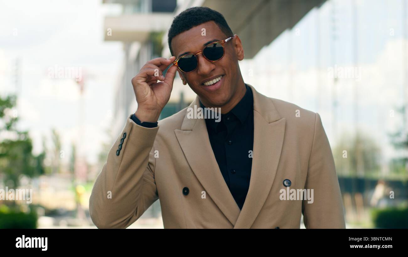 Smiling stylish fashionable confident African American business man posing in city outdoors wearing black sunglasses businessman guy male entrepreneur Stock Photo