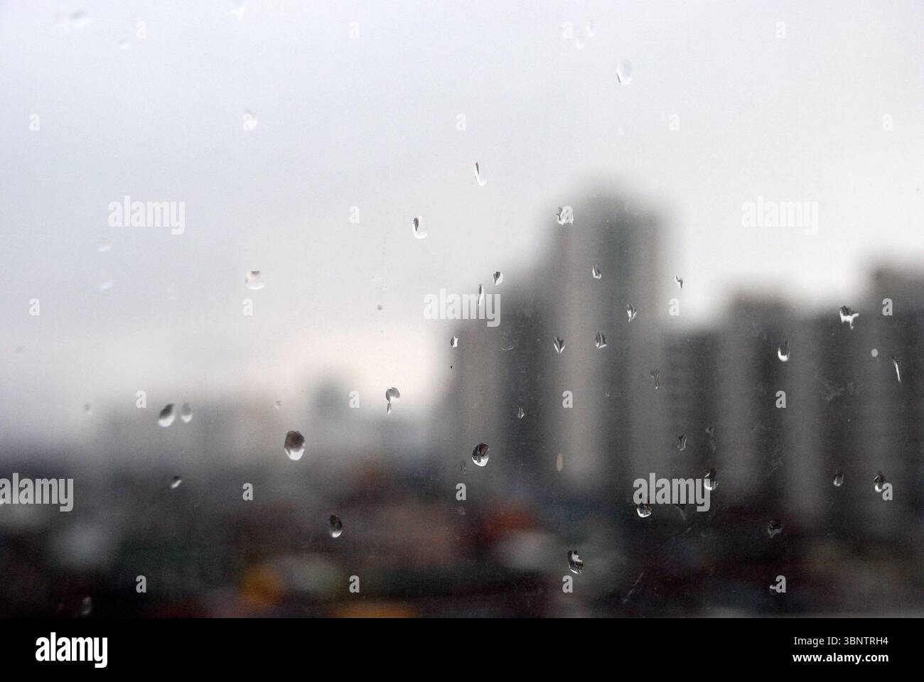 Rainy city view through window with raindrops Stock Photo