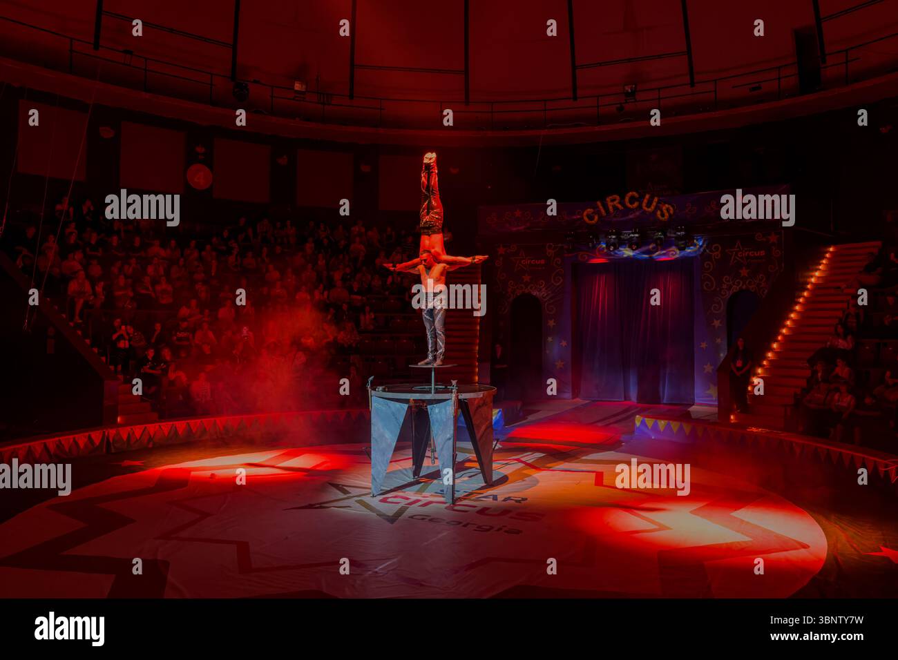 Partner hand-to-hand acrobatics on a raised platform during a circus show in Batumi, Georgia. Night performance with audience. Editorial use only. Stock Photo