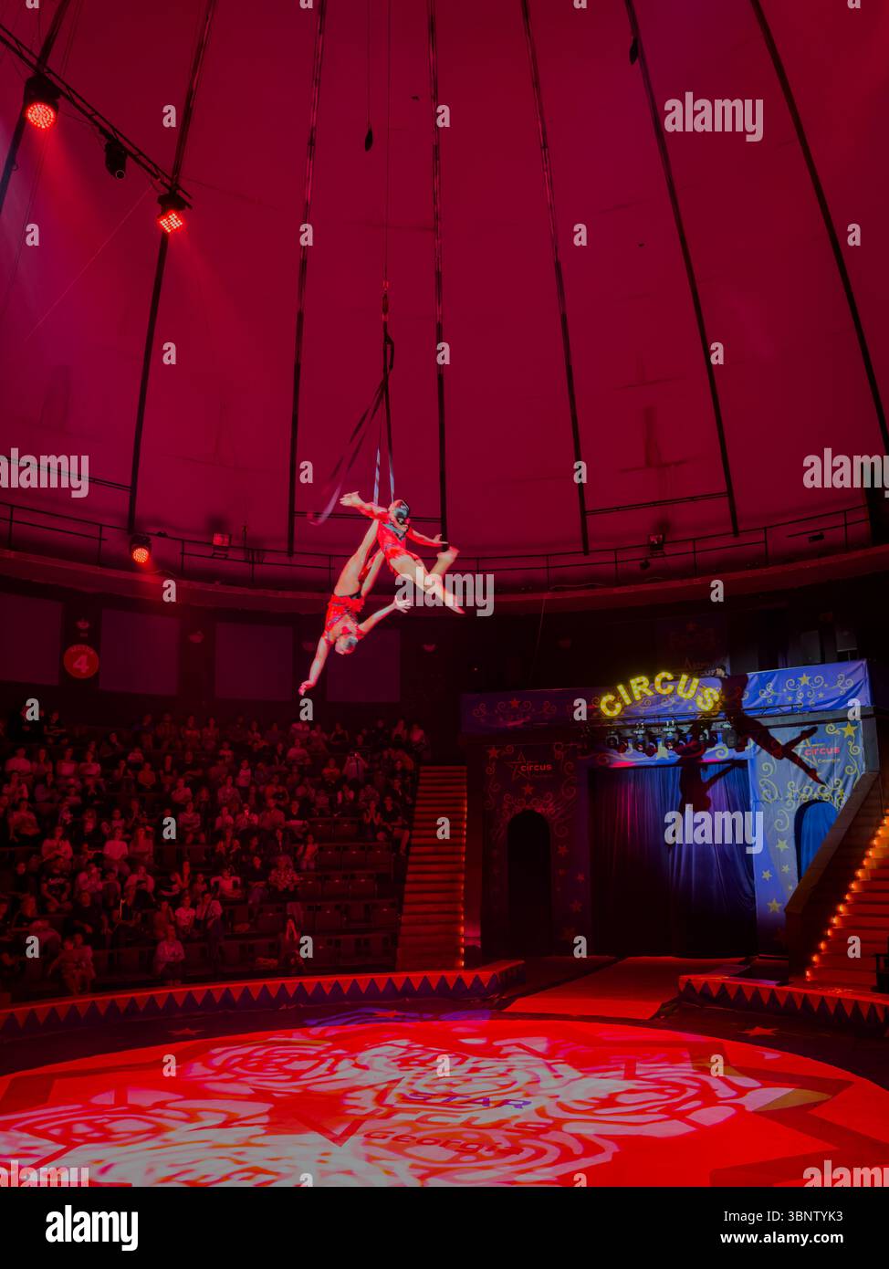 Aerial straps duet performance during a circus show in Batumi, Georgia. Acrobats suspended mid-air under dramatic lighting. Editorial use only. Stock Photo