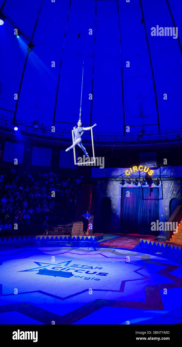 Female aerialist performing on a suspended frame during a circus show in Batumi, Georgia. Strong theatrical blue lighting. Editorial use only. Stock Photo