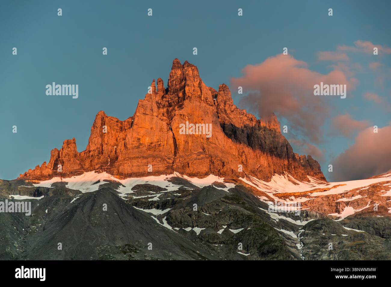 Alpenglow on the Großer Spannort, evening atmosphere on the Hobiel Alp. From the Hobiel Alp, the Großer Spannort appears as a striking rock tower  towering above the Spannort Glacier and the Glattfirn. Alpenglow on the Spannort mountain. Majestic mountain peaks in the Swiss Alps, illuminated by the warm light of the setting sun. The scene shows the rugged rocks and snowfields in the Engelberg region, Canton Uri, Switzerland, near Hobiel Alp, Europe, while pink clouds loom in the sky Stock Photo