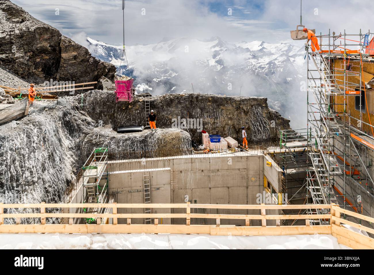 It is expected to be the largest construction site in the Alps until 2029, with construction cranes, excavators and concrete mixers. The major "Titlis 3020" project includes the construction of a new mountain station at an altitude of 3,020 metres and the expansion of a new cable car and shops for purchasing luxury goods. Construction workers carry out challenging building work on the Titlis in Engelberg, Obwalden, Switzerland. A crane and an excavator are used to move materials in the rocky high mountain landscape. The work is taking place amidst snow-covered peaks and clouds to expand the to Stock Photo