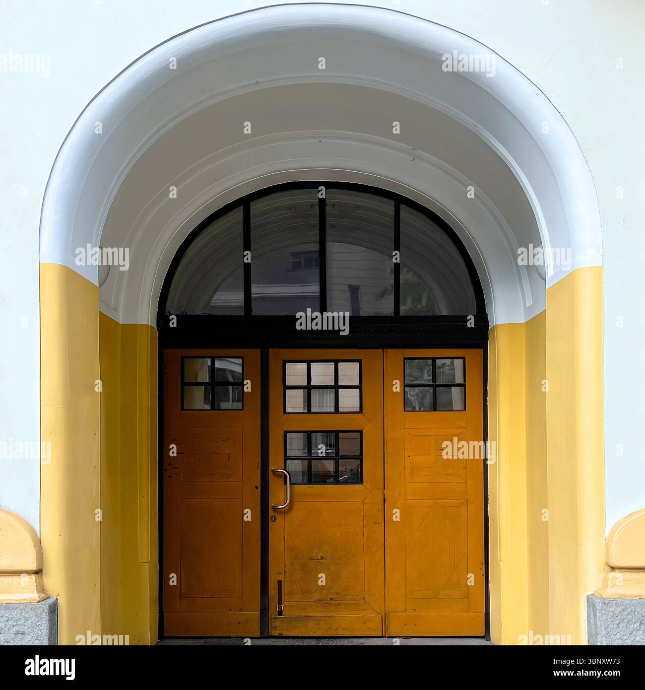 A boldly painted yellow wooden door set beneath a graceful arched entryway in Warsaw, Poland, showcases a blend of vintage charm and architectural sym - Smartphone Captured Stock Image
