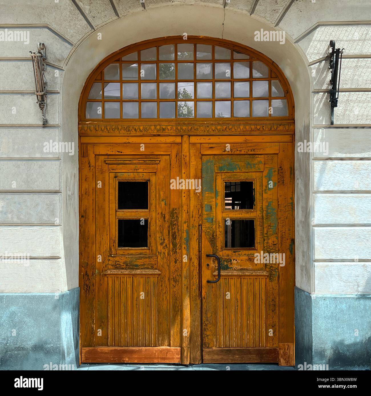 A timeworn golden-yellow door in Warsaw, Poland, reveals layers of peeling paint and patina under a decorative arched transom. - Smartphone Captured Stock Image