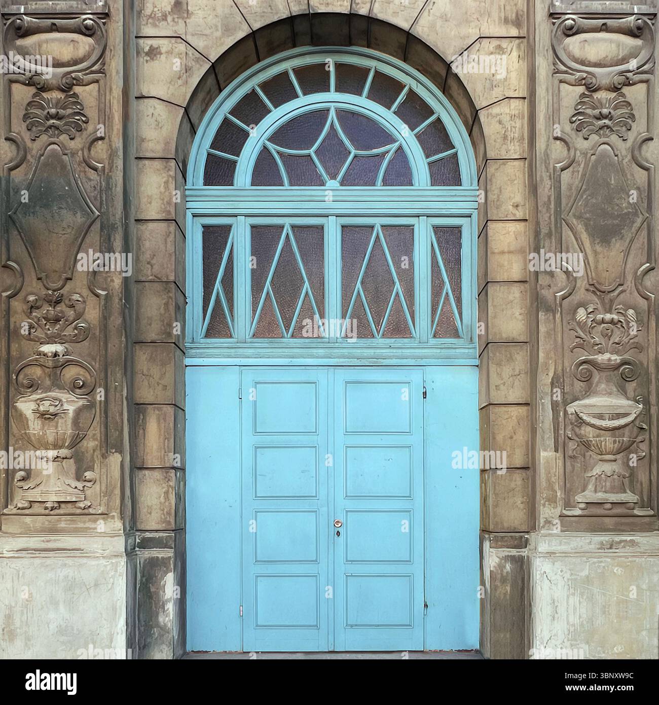 A pale blue neoclassical door in Warsaw framed by ornate stonework and topped with a diamond-paned fanlight, blending elegance with historic charm. - Smartphone Captured Stock Image