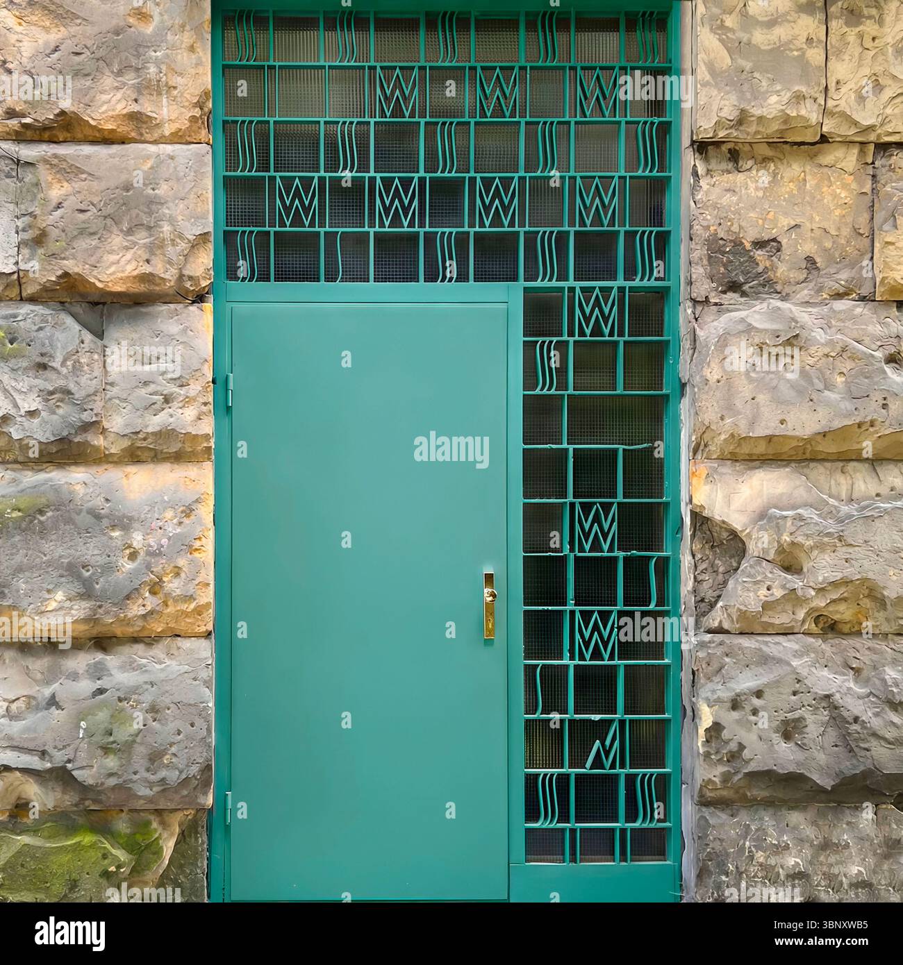 A mint green interwar-era door from 1930s Warsaw, Poland, features a geometric grille and streamlined modernism set in a rough-hewn stone facade. - Smartphone Captured Stock Image