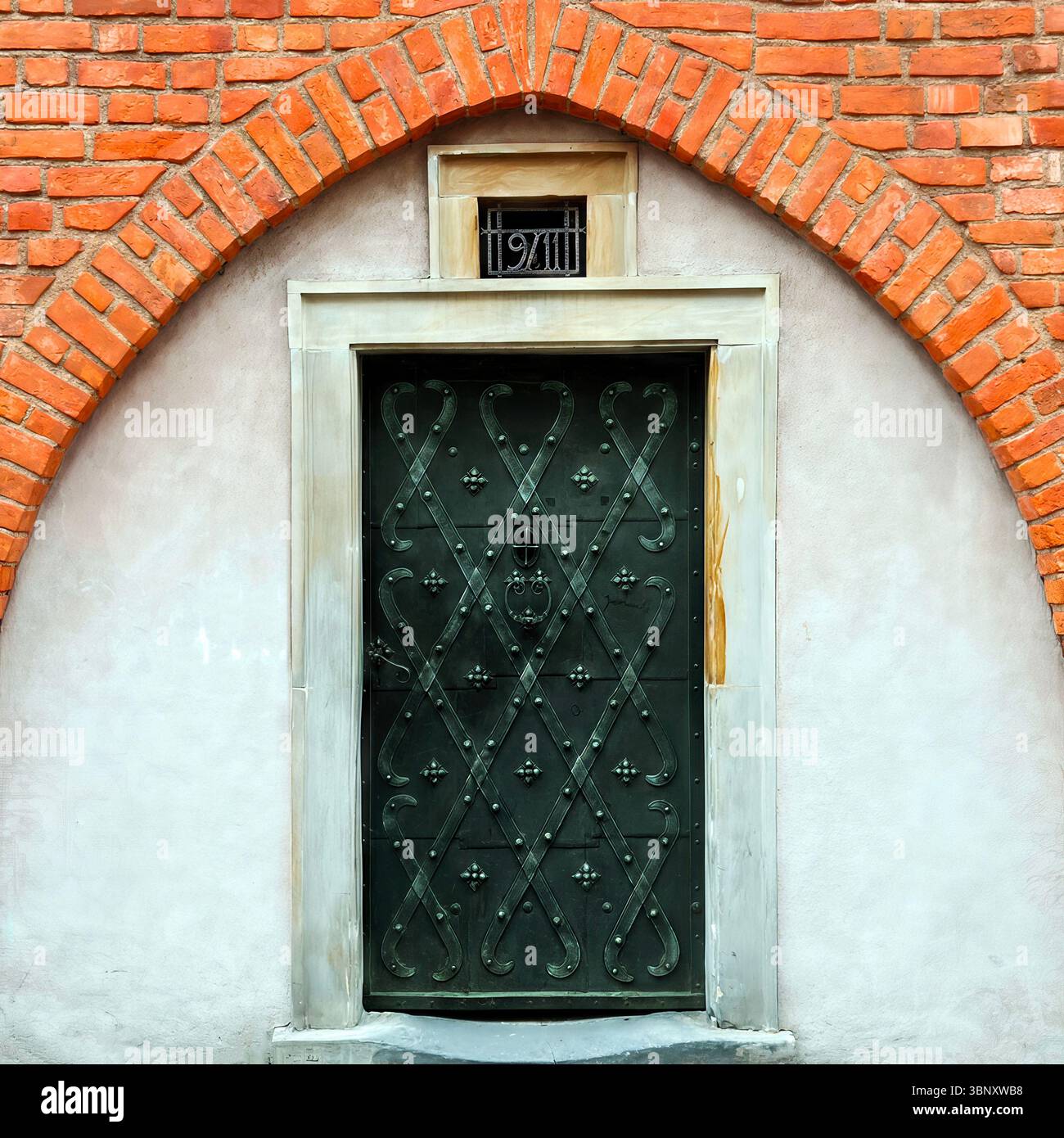 A dark green wrought iron door in Warsaw’s Old Town stands beneath a red brick Gothic arch, echoing strength and artistry in historic stonework. - Smartphone Captured Stock Image