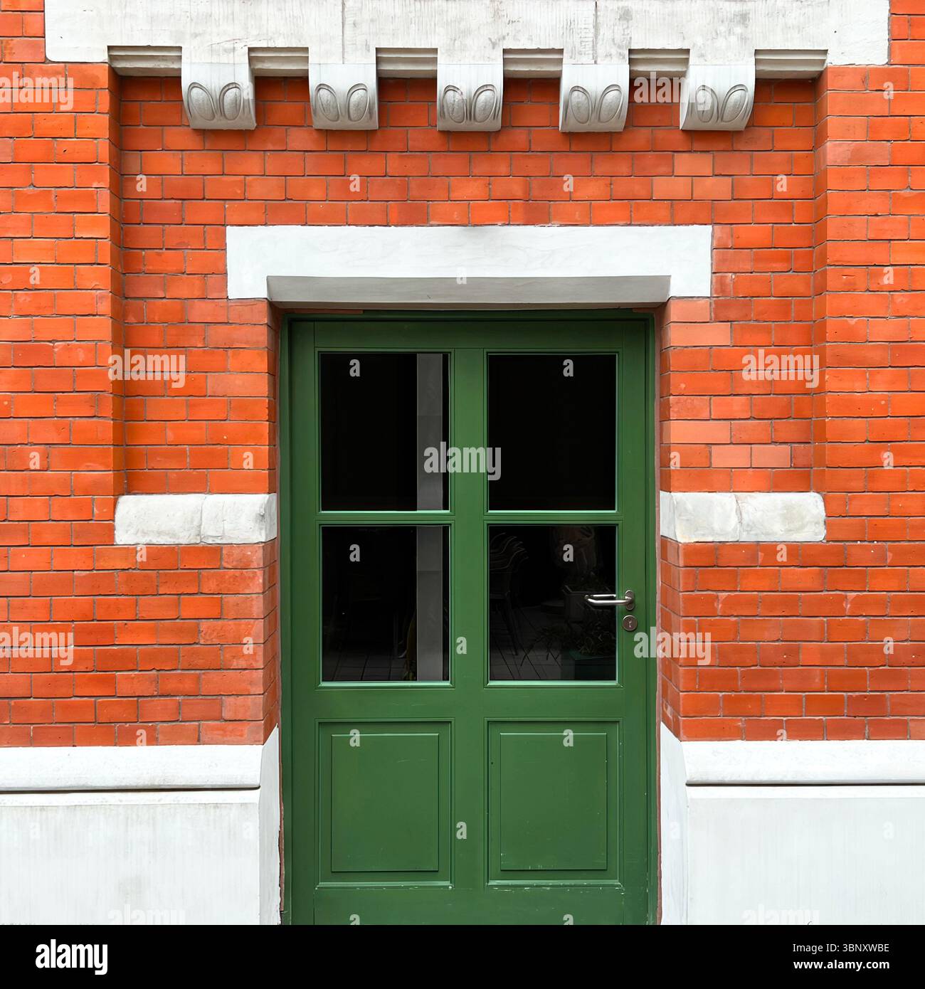 A green-paneled door with modern glazing opens to the courtyard of Hala Koszyki in Warsaw, framed by restored red brickwork and white detailing - Smartphone Captured Stock Image
