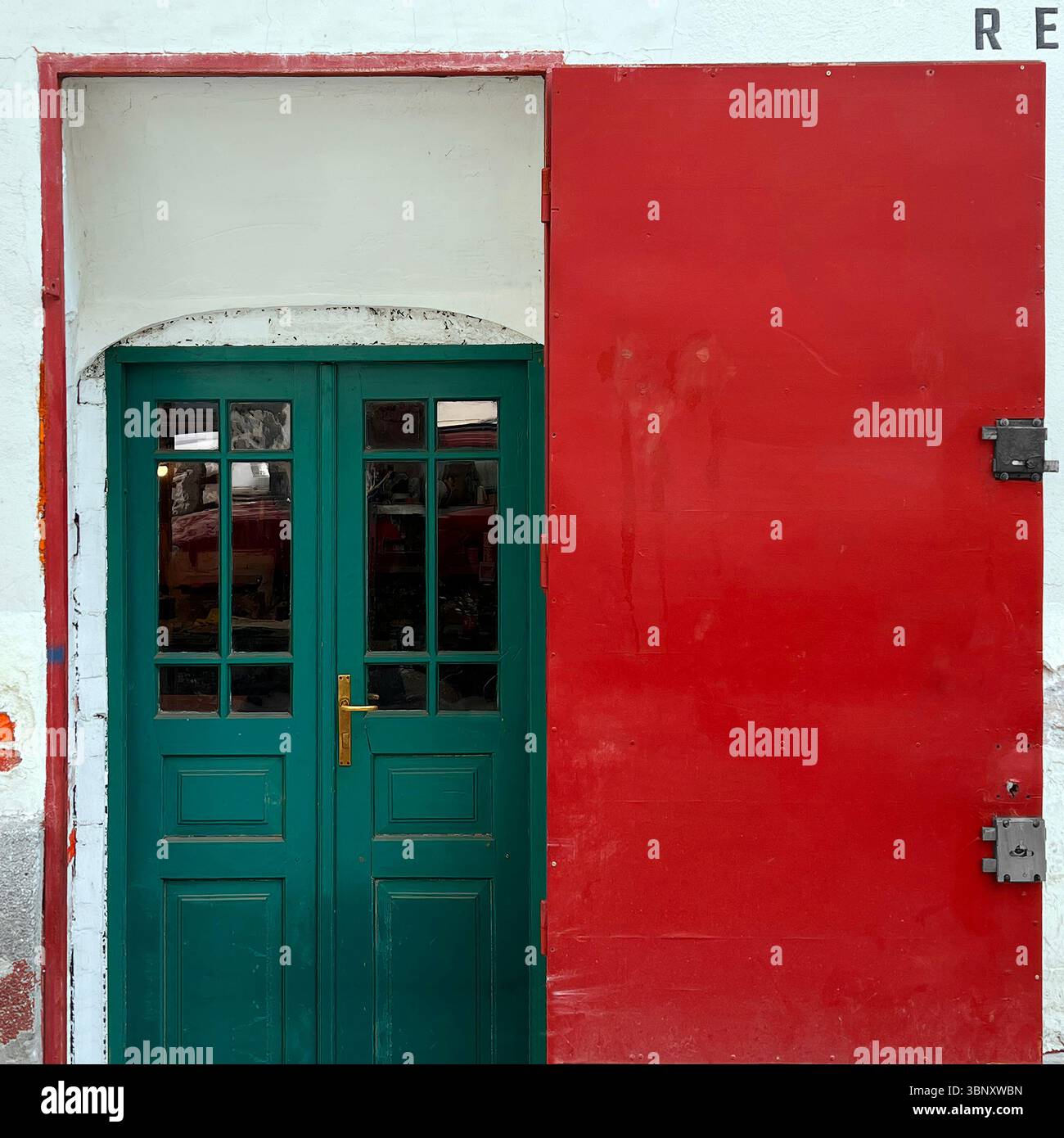 A green double door with golden hardware pops against a bold red panel on a Warsaw storefront—an eye-catching clash of color, texture. - Smartphone Captured Stock Image