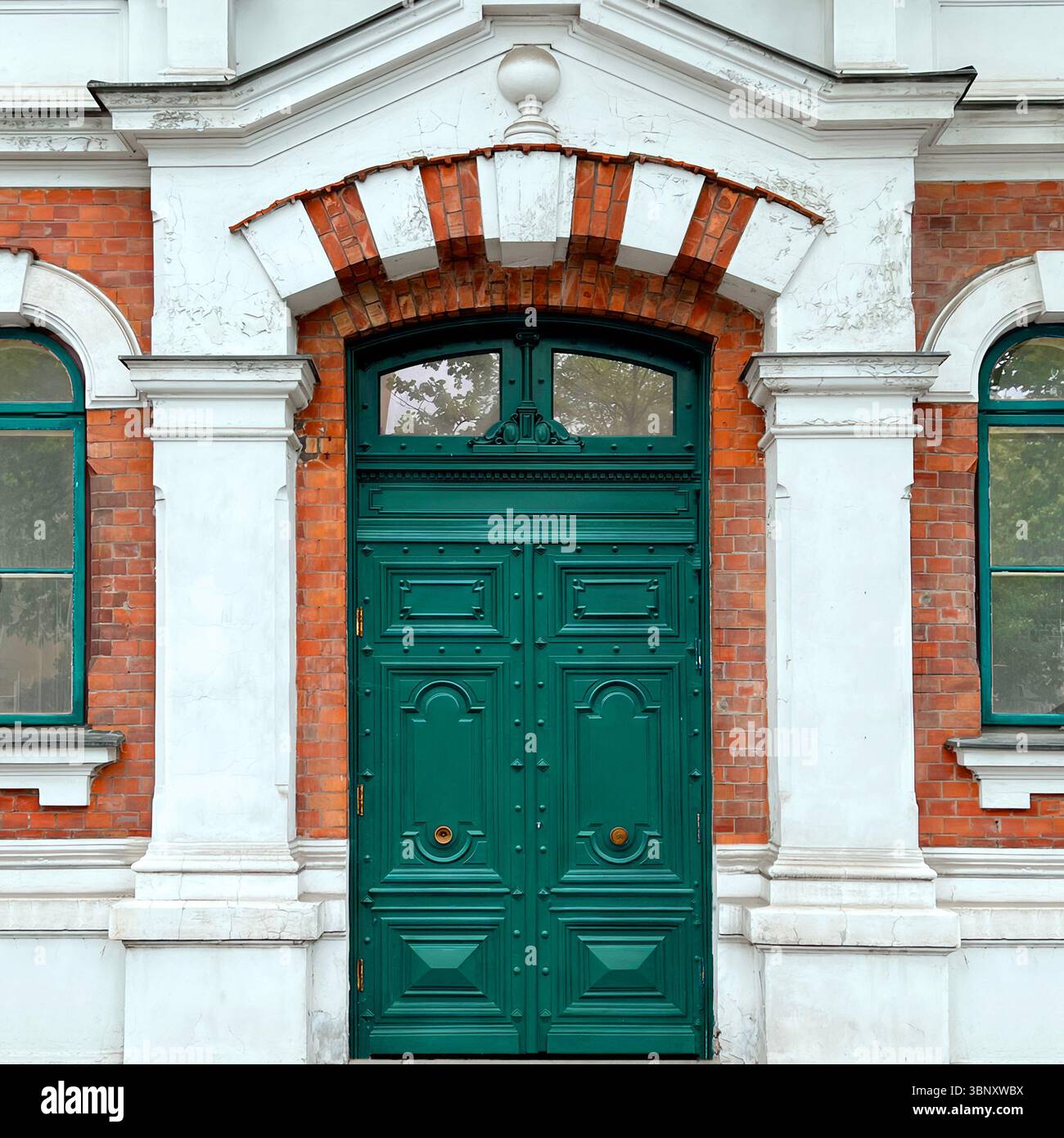 An ornate green double door in Warsaw is framed by red brick, white plaster, and a pedimented arch—an elegant echo of 19th-century architectural pride. - Smartphone Captured Stock Image