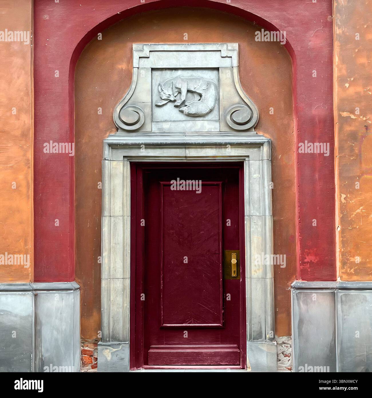 A dark red door in Warsaw’s Old Town rests beneath a carved fox relief, framed by stone and ochre walls—blending folklore with architectural dignity. - Smartphone Captured Stock Image