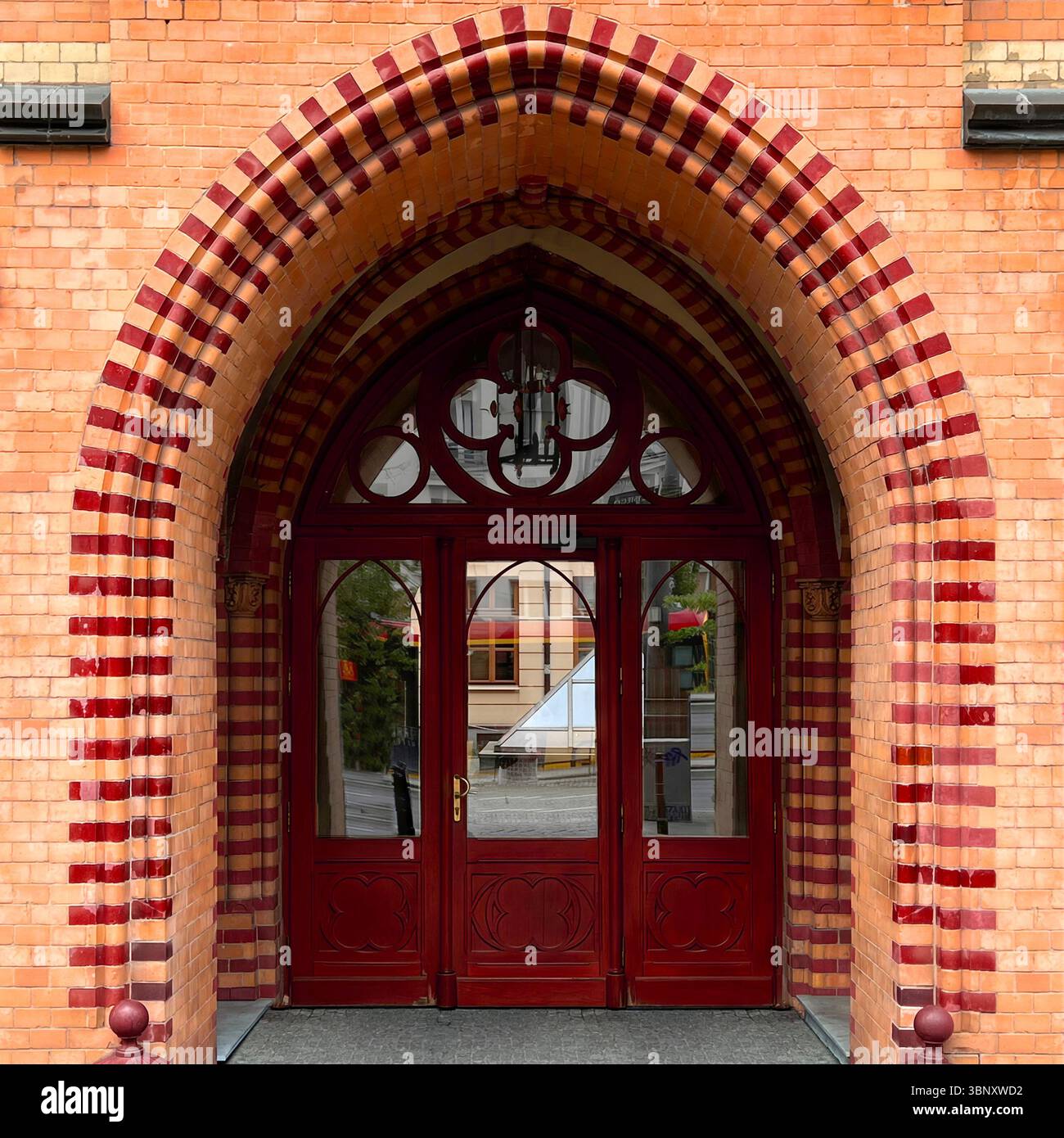 Gothic-inspired arch frames a richly detailed red door in Warsaw, blending ornamental brickwork with graceful symmetry and historic charm. - Smartphone Captured Stock Image