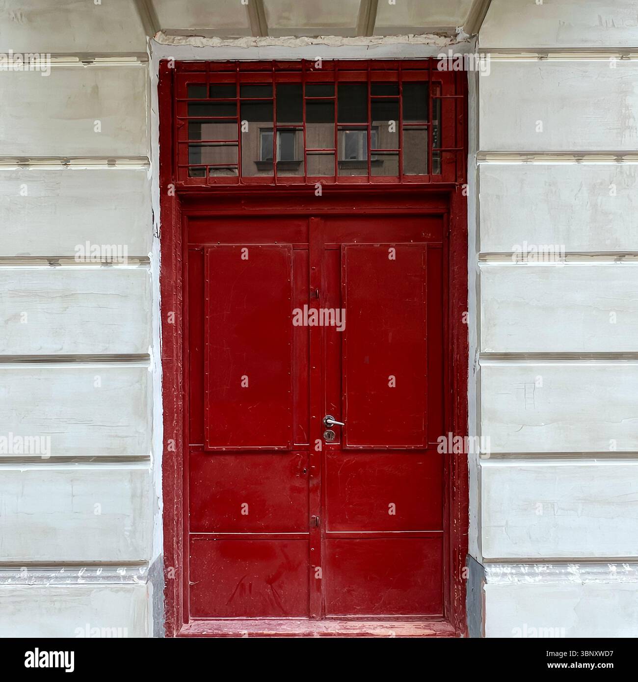 A bold red metal door with a barred transom stands out against a pale neoclassical facade in central Warsaw. - Smartphone Captured Stock Image