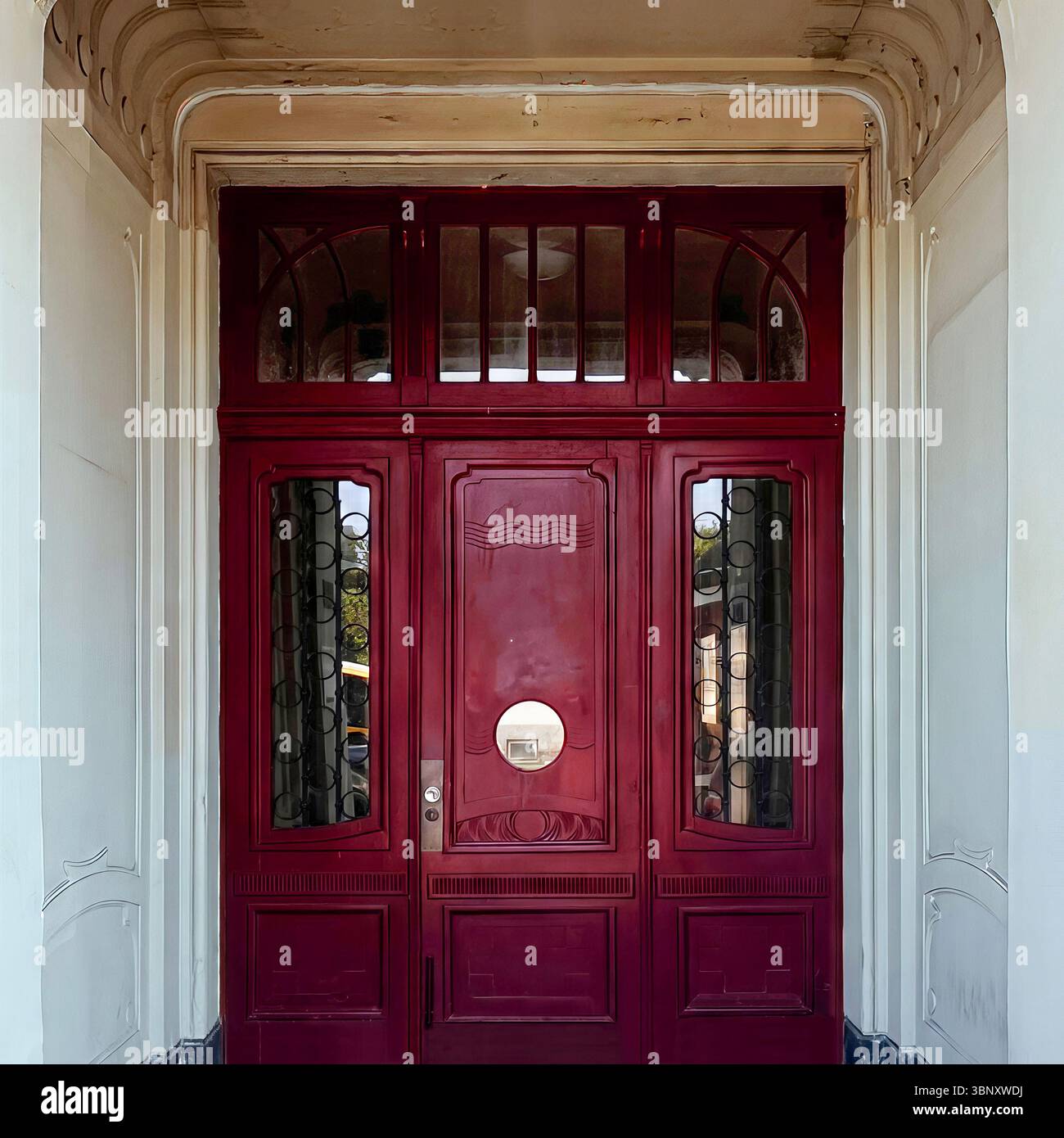 Elegant red Art Deco doorway framed by curved molding and patterned glass panels in central Warsaw. - Smartphone Captured Stock Image