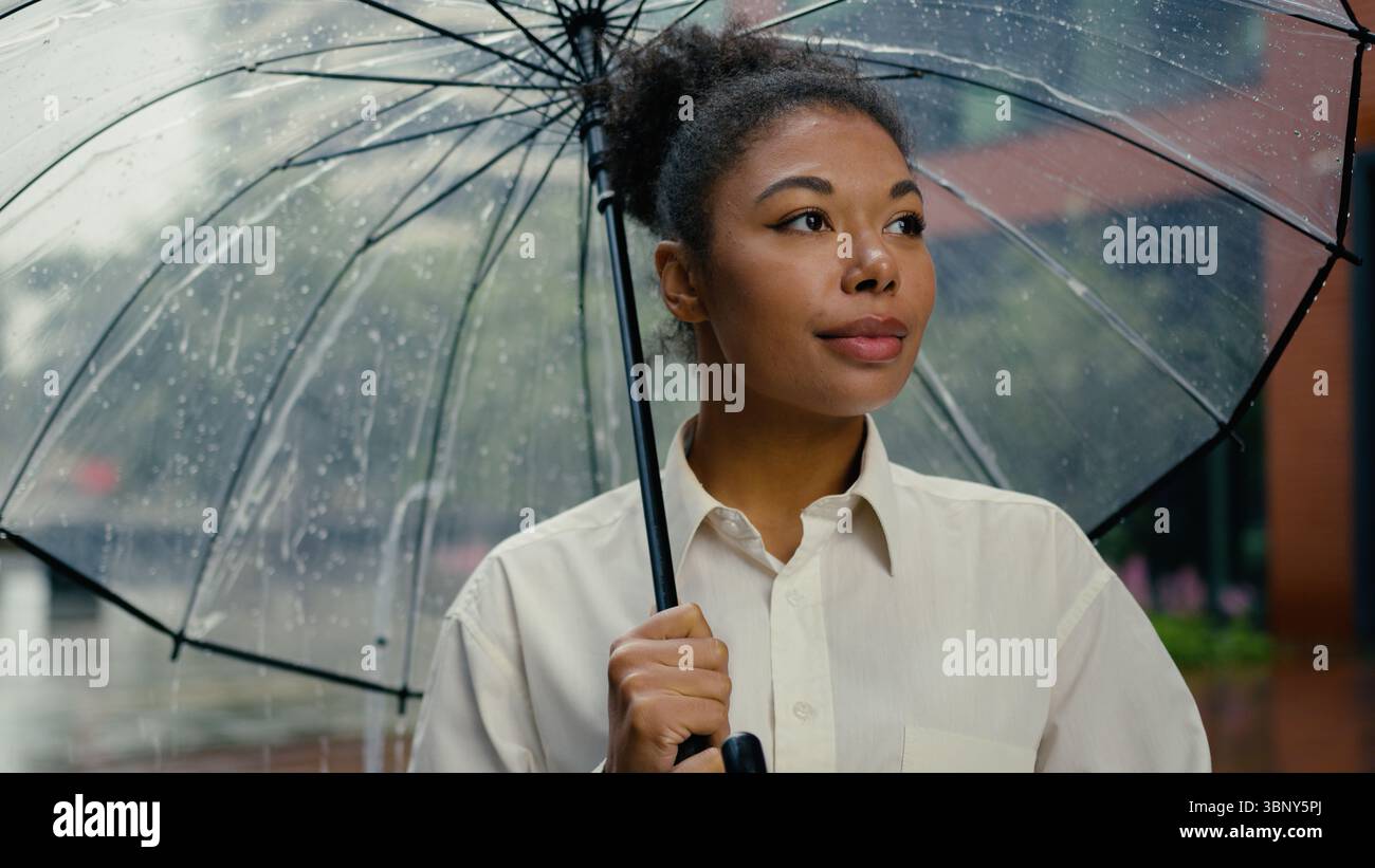 Successful African American woman looking at camera smiling worker holding umbrella rain female girl businesswoman business city leader employer Stock Photo