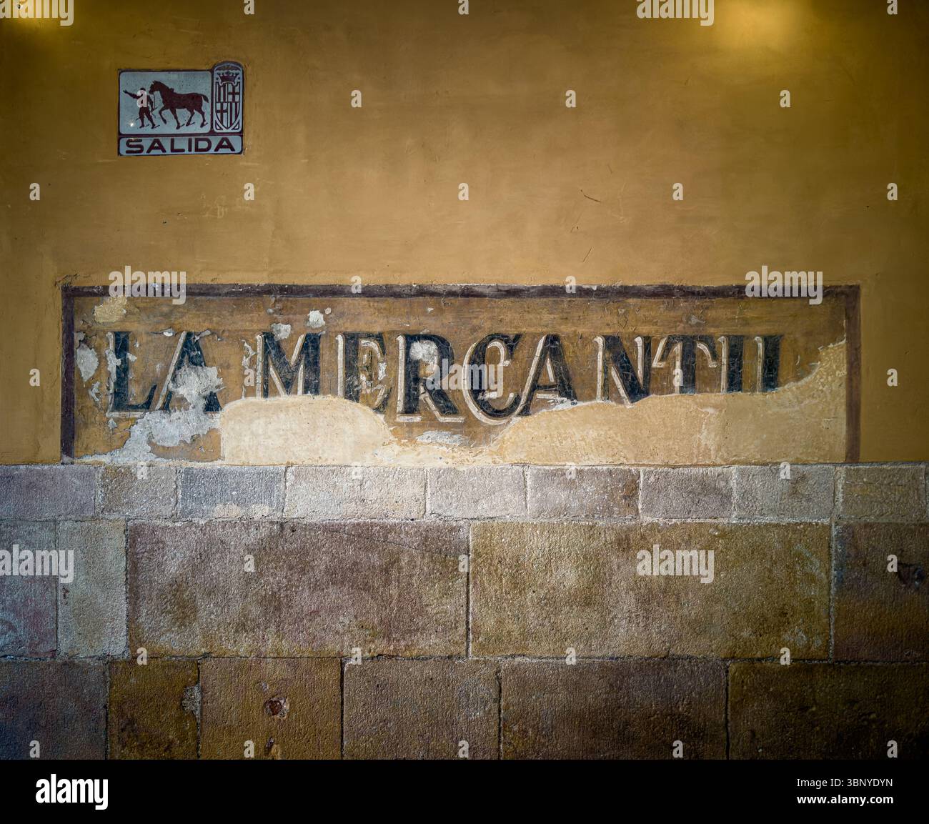 Faded ‘La Mercantil’ ghost sign on aged wall, with historic ‘Salida’ plaque once guiding carts through Barcelona’s Ciutat Vella streets. Stock Photo