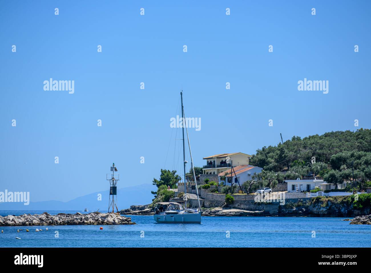 12-19/05/2025  Gaios, Paxos, Greece. Yacht slowly motoring through the harbour entrance, with a large villa on the right and a harbour marker on the left. Photo © Simon Grosset Stock Photo