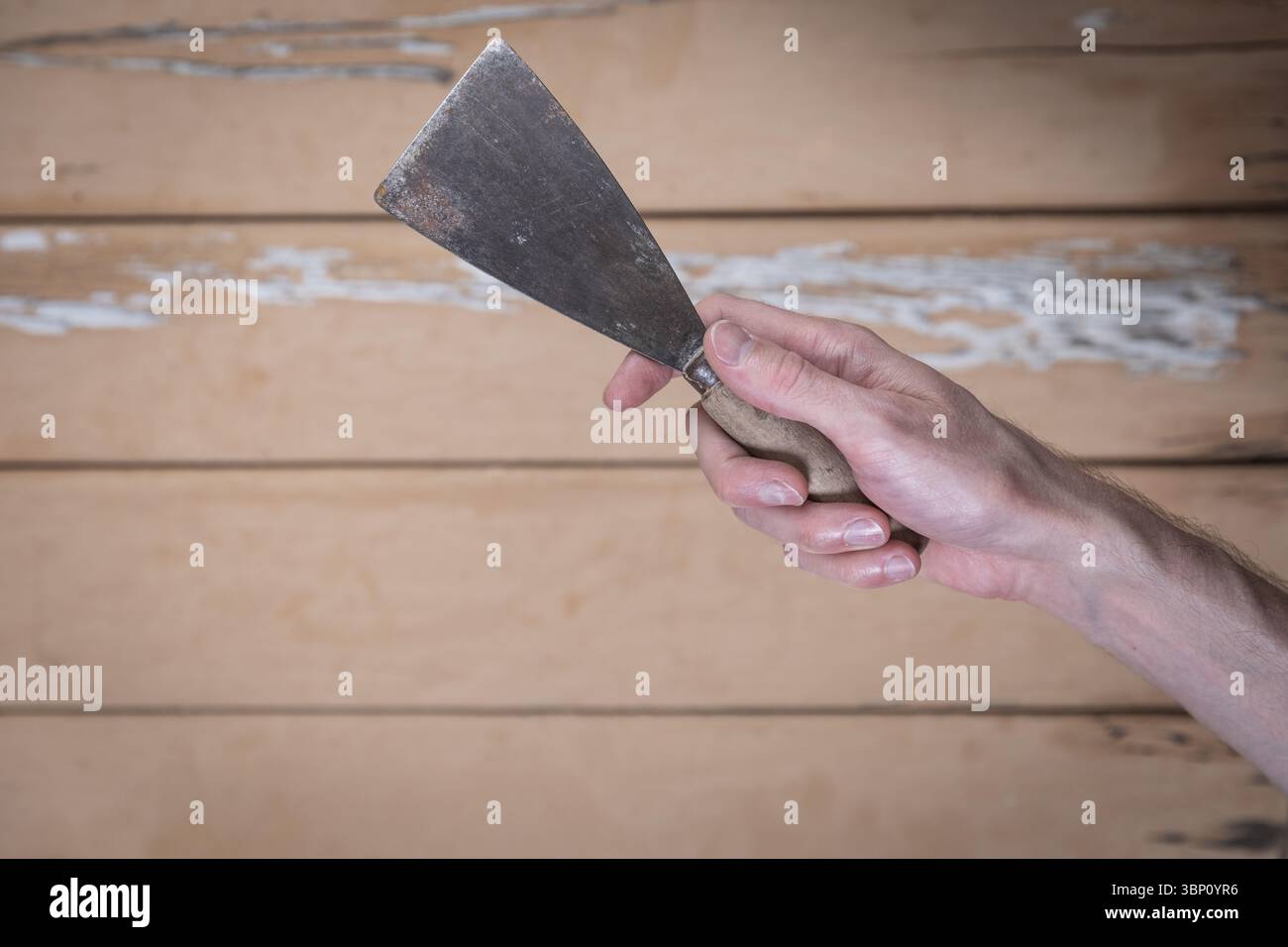 Top-down view of a hand holding a worn metal scraper with wooden handle ...