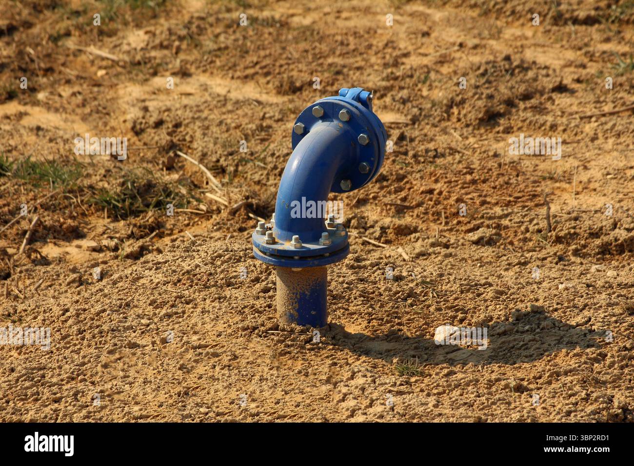 A blue water pipe with bolts and a curved joint emerges from dry ...