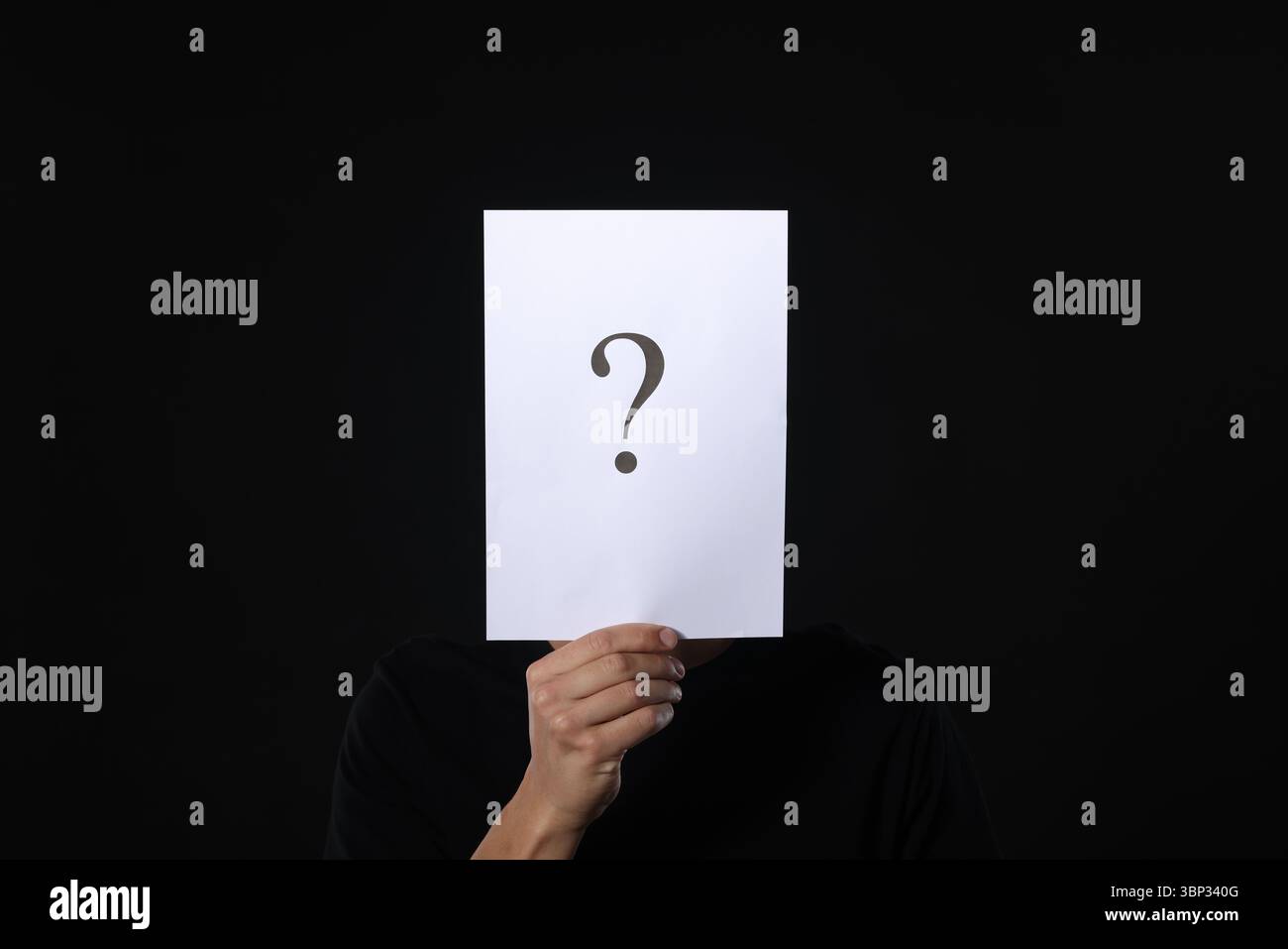 Man hiding behind paper sheet with question mark on dark background Stock Photo