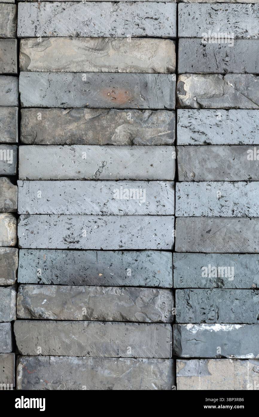 Stacked gray rectangular concrete bricks create detailed geometric pattern. Varying in shades and textures, weathered blocks form industrial scene. Stock Photo