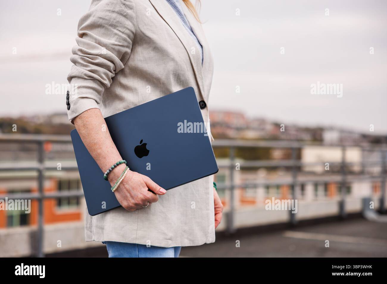 Zlin, Czech Republic - April 13, 2025: Businesswoman with Apple laptop MacBook Air walking outside of office building Stock Photo