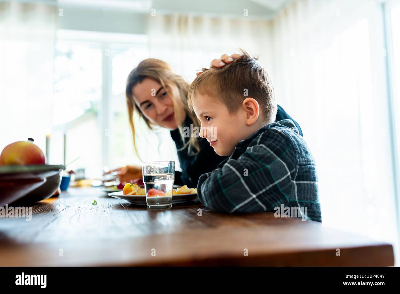 Mother caressing son eating lunch at dining table Stock Photo