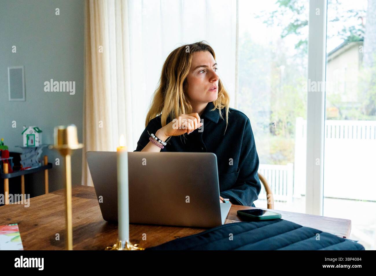 Female freelance worker looking away while sitting with laptop on table at home office Stock Photo
