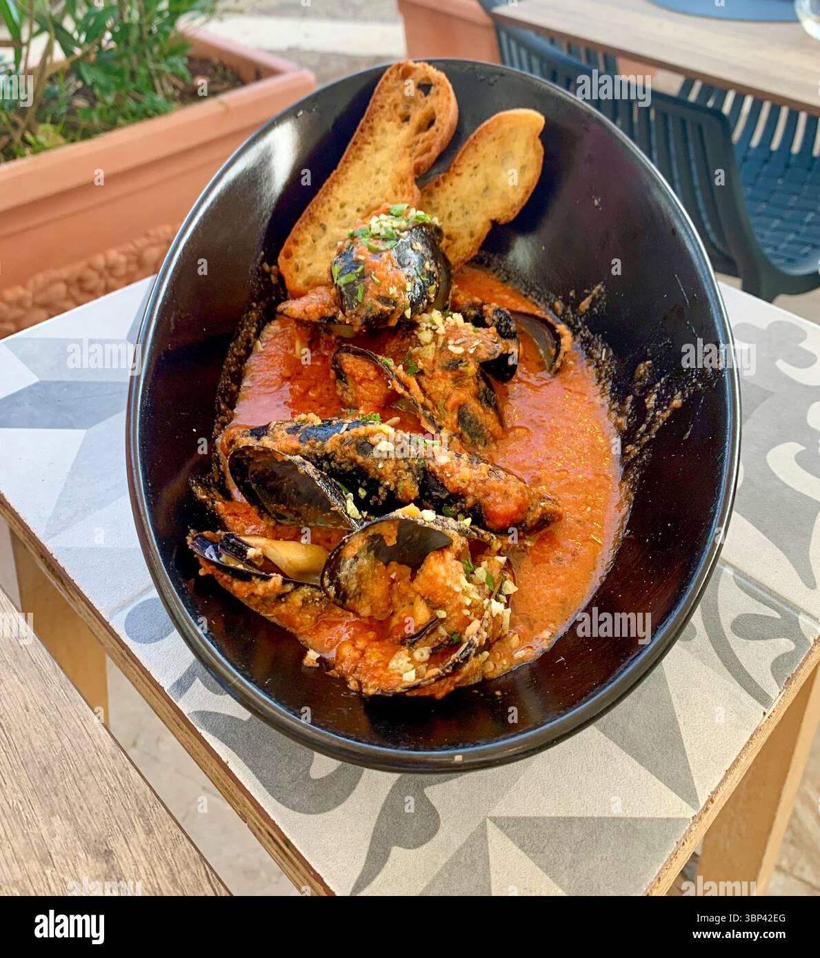 A flavourful close-up of the mussels starter from ALevante in Ortigia, Italy-tender mussels in a rich, aromatic broth, served with crisp garlic bread. Stock Photo