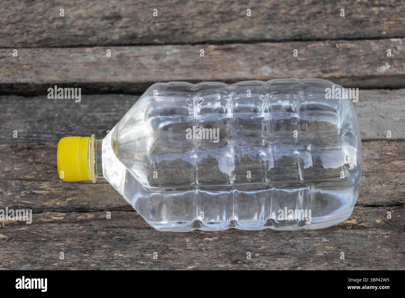 Plastic water bottle with yellow cap lying on rustic wooden surface Stock Photo