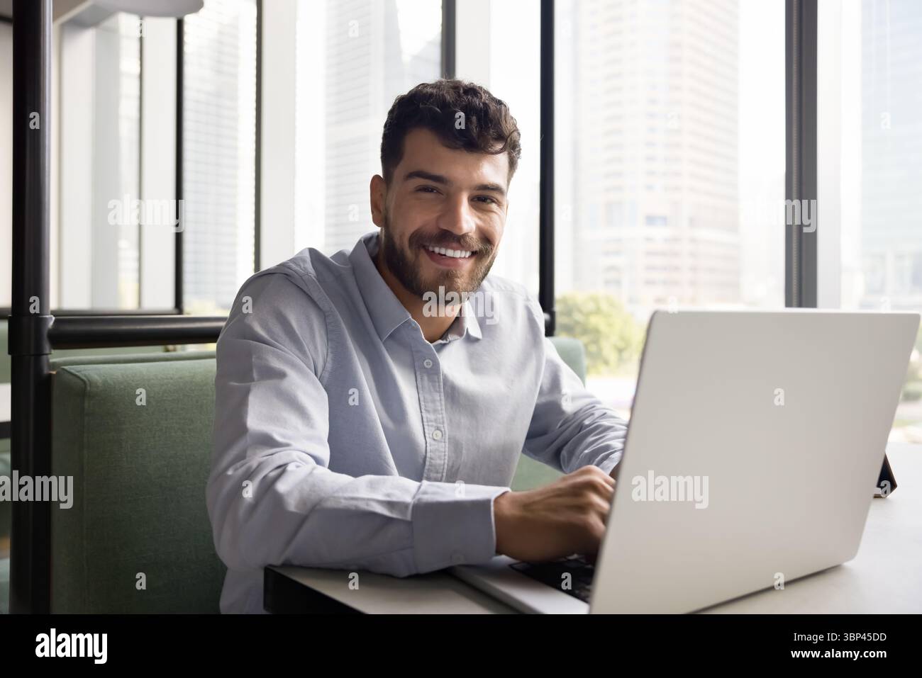 Happy millennial male using notebook at cafe looking at camera Stock Photo