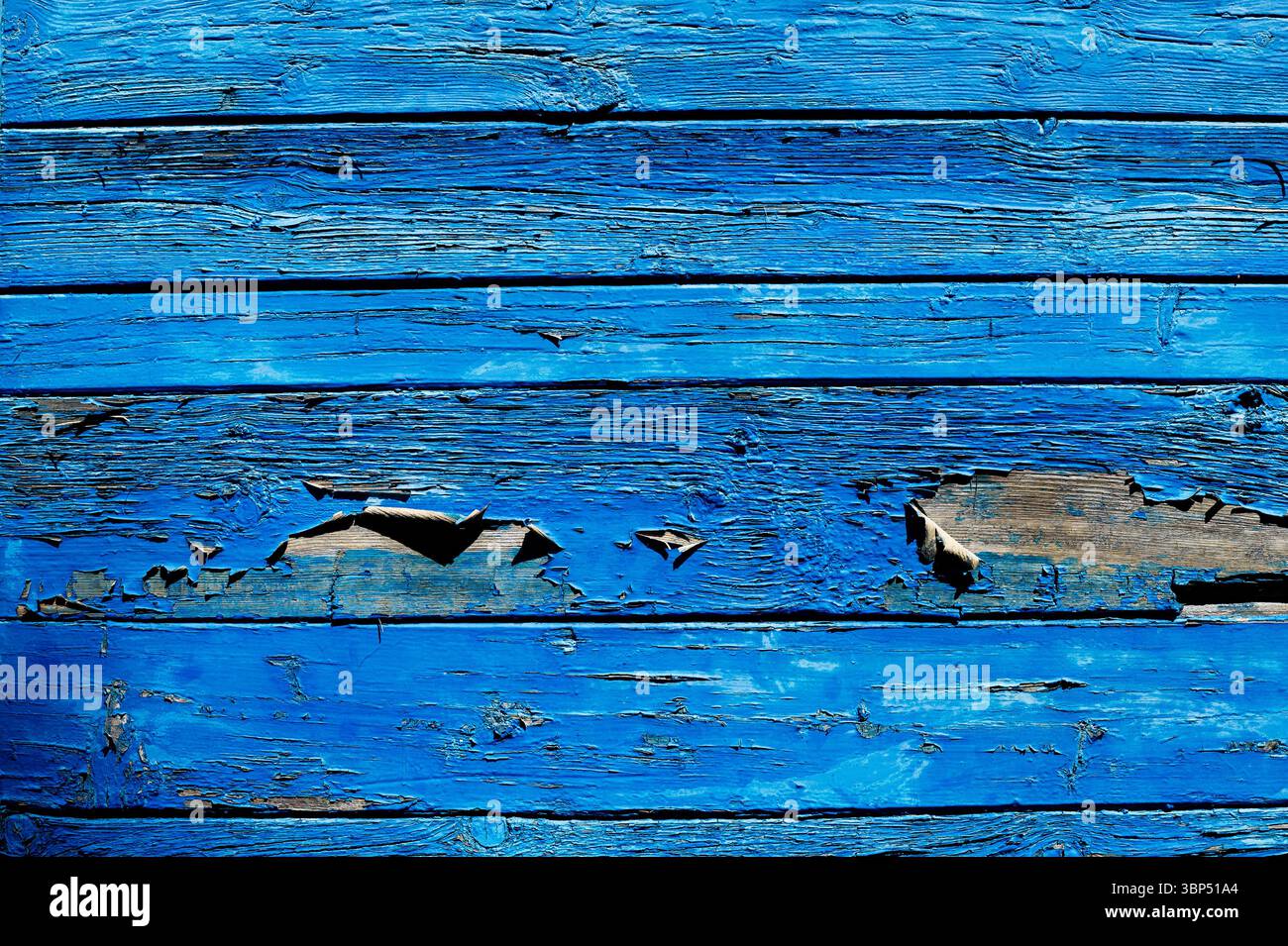 Close up of weathered blue painted wooden planks, revealing the natural wood grain beneath the chipped paint, creating a textured and rustic backdrop Stock Photo